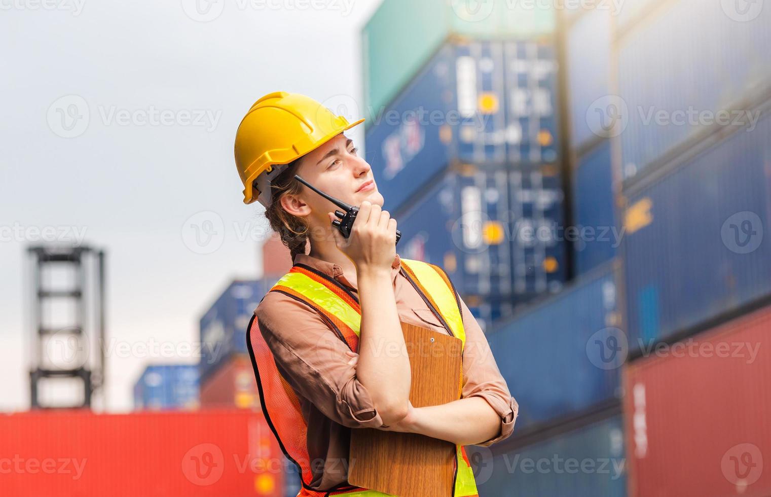 Engineer in hardhat and safety vest holding clipboard checklist and two-way radio at containers cargo photo