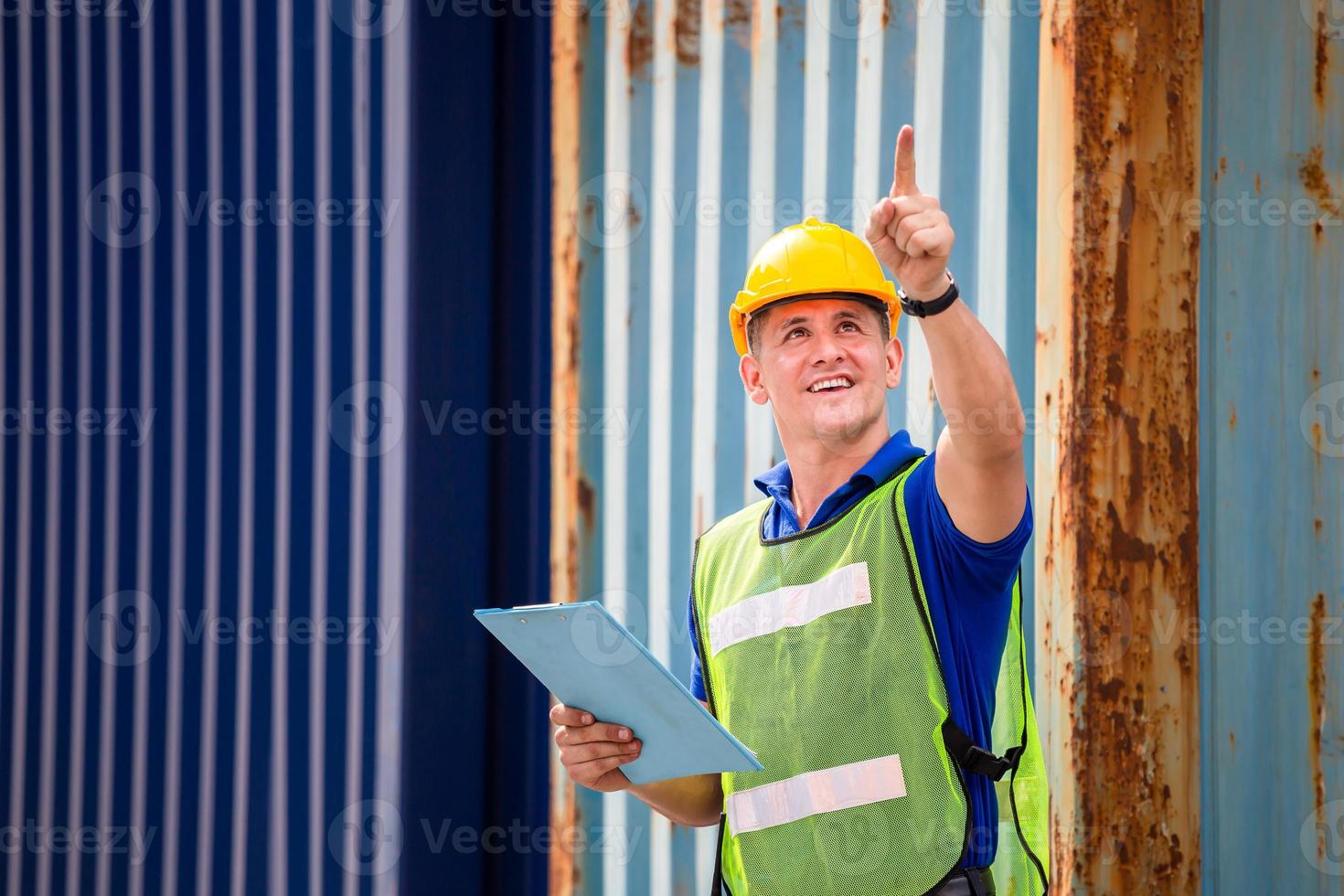 Foreman worker in hard hat and safety vest smiling and pointing control loading containers box from cargo photo