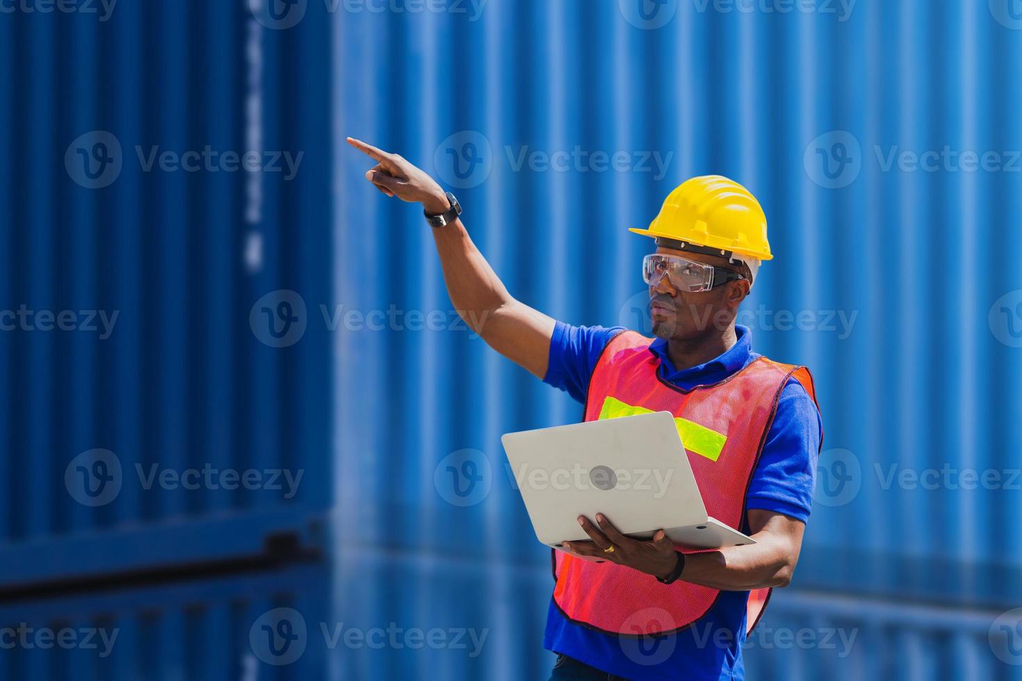 Engineer with clipping path in hard hat and safety vest holding a laptop, Factory worker man at container cargo photo