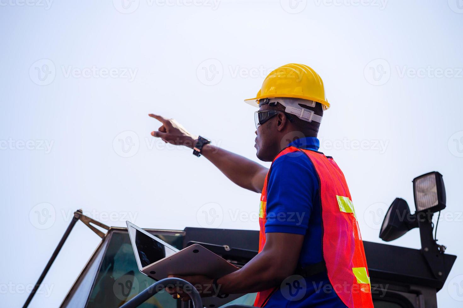 Worker man in hardhat and safety vest holding laptop standing on container stackers control loading containers box from cargo photo