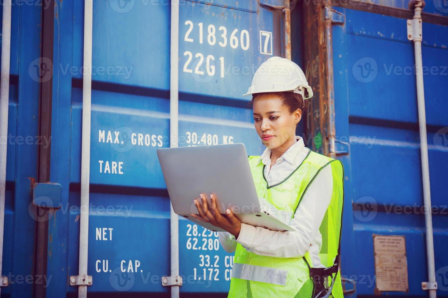 Female engineer in hardhat and safety vest holding laptop, Foreman control loading containers box from cargo photo