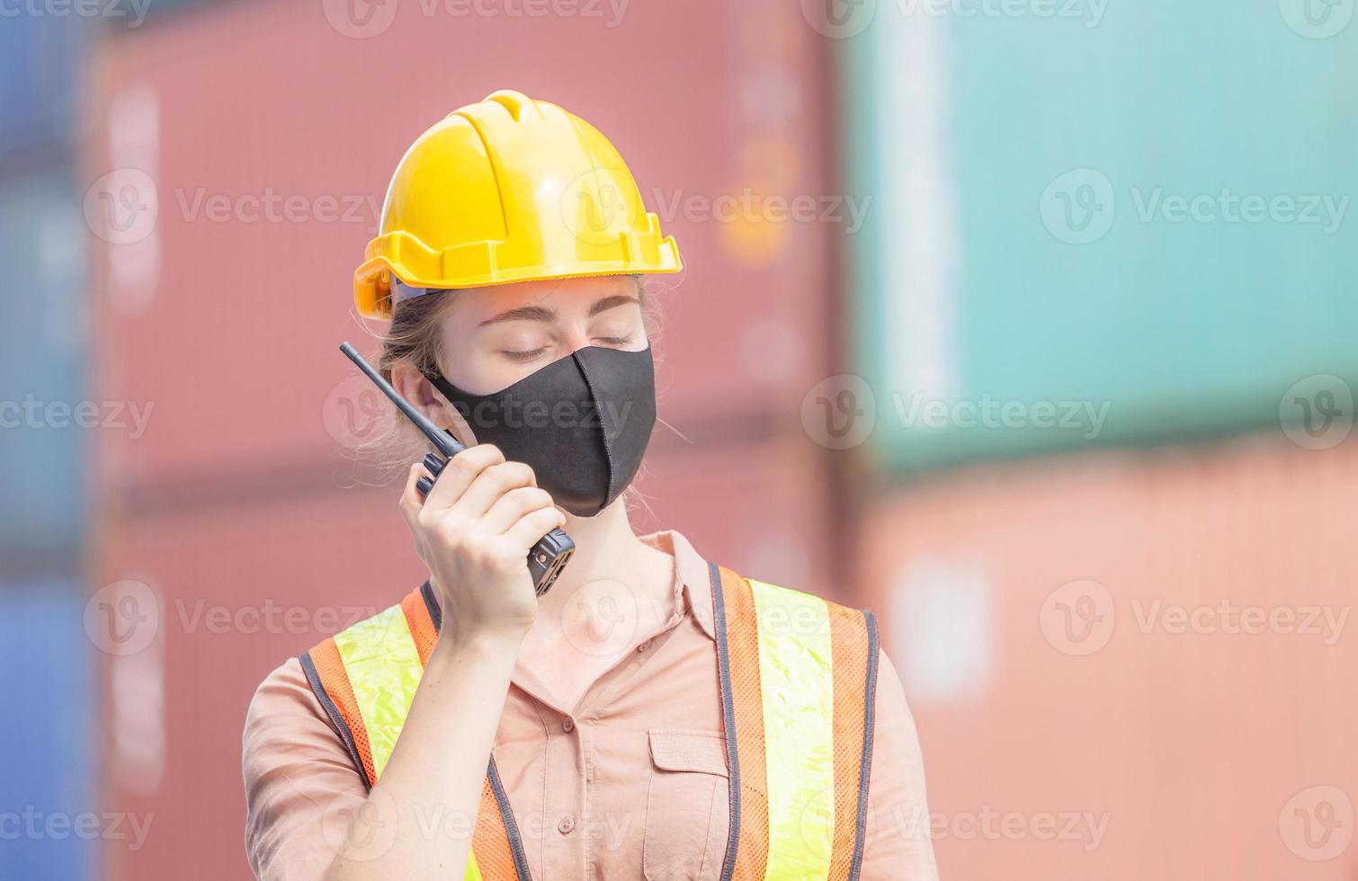 Woman Foreman in hardhat and safety vest holding holding clipboard checklist and talks on two-way radio control loading containers box from cargo photo