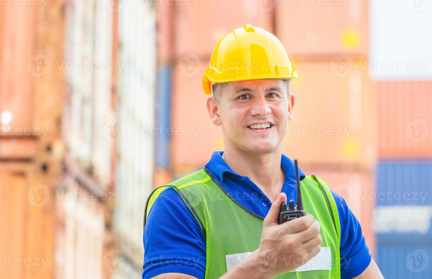 Happiness foreman in hardhat and safety vest talks on two-way radio control loading containers box from cargo photo