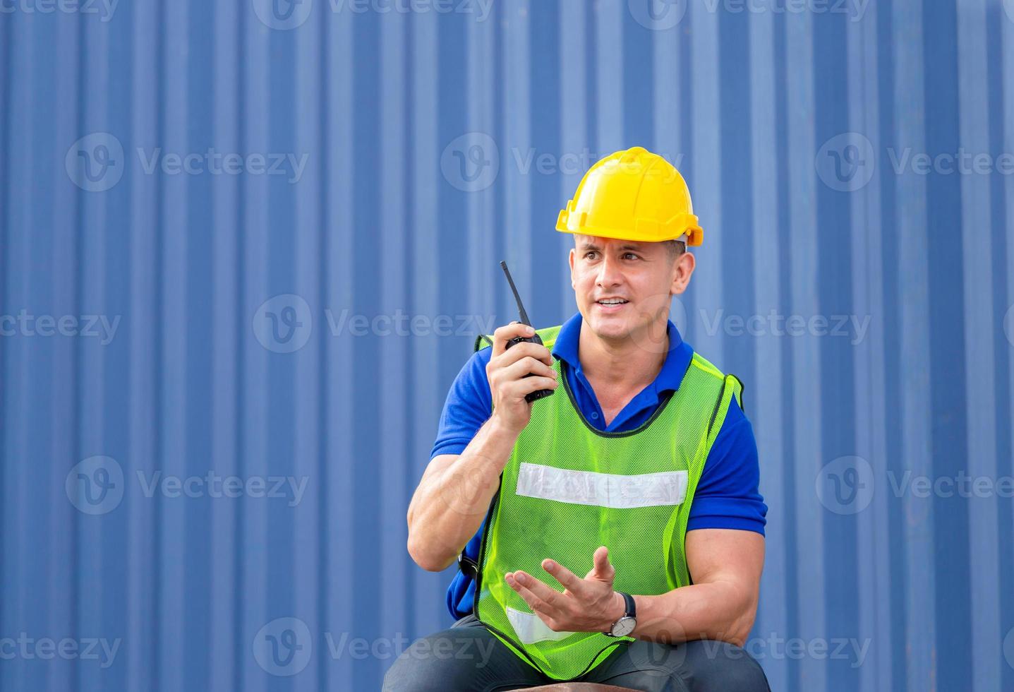 Foreman worker in hardhat and safety vest sitting on container box, engineer talks on two-way radio control loading containers box from cargo photo