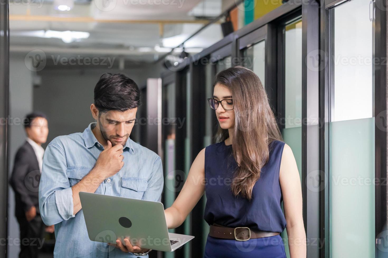 un joven hombre de negocios que sostiene una laptop y camina discute el trabajo con un equipo femenino, un equipo de negocios de compañeros de trabajo reunidos en una oficina creativa foto