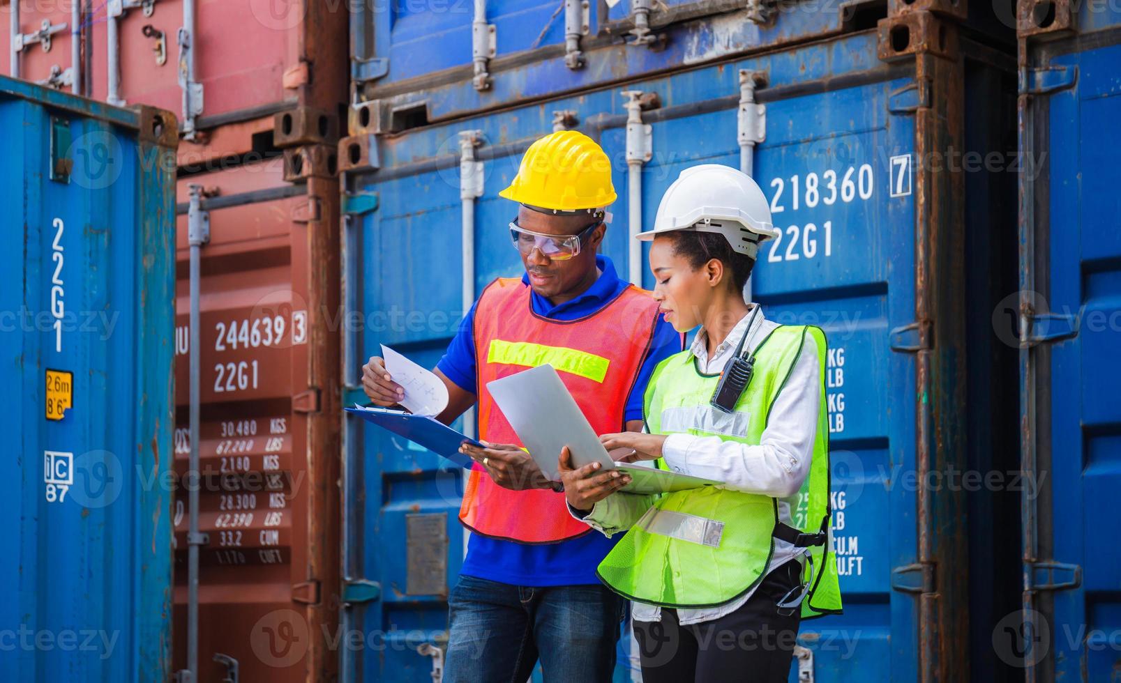 Worker man in hardhat and safety vest holding clipboard checklist and Female foreman using laptop control loading containers box from cargo photo