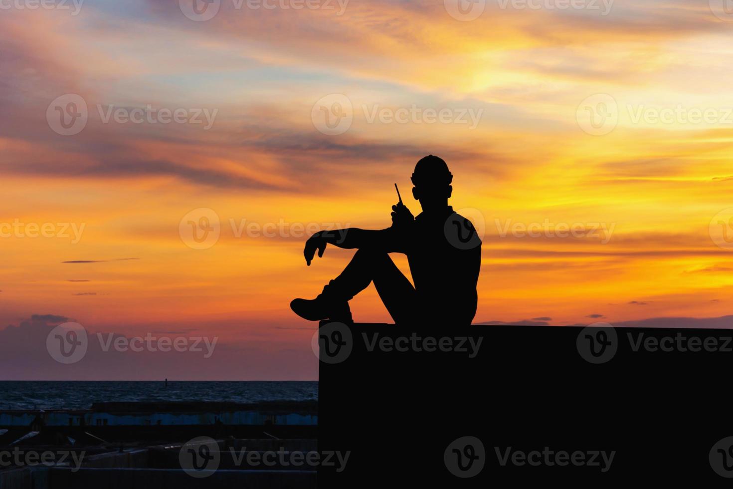 Silhouette of Foreman in hard hat sitting on container box with sunset sky photo