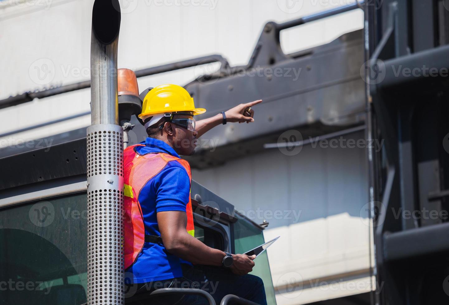 Worker man in hardhat and safety vest holding laptop standing on container stackers control loading containers box from cargo photo