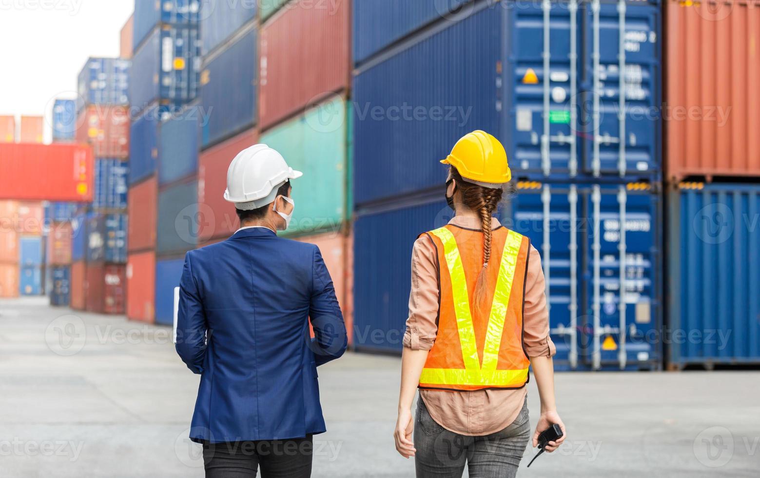 Engineer in hardhat and safety vest together talking with foreman worker wearing protection face mask against coronavirus at containers cargo photo