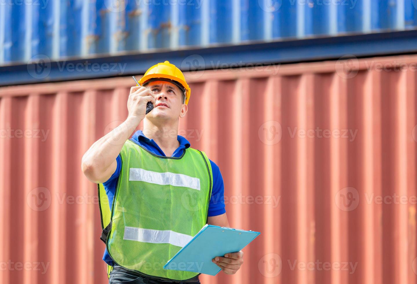 Foreman in hard hat and safety vest talks on two-way radio at containers cargo photo
