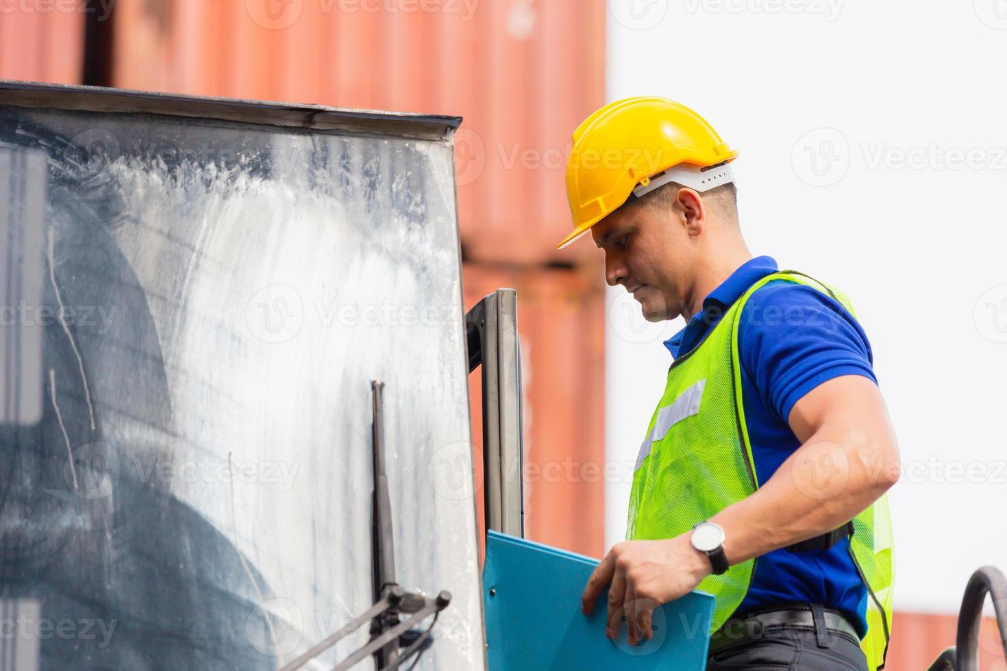 Worker man in hard hat and safety vest standing on container stackers control loading containers box from cargo photo