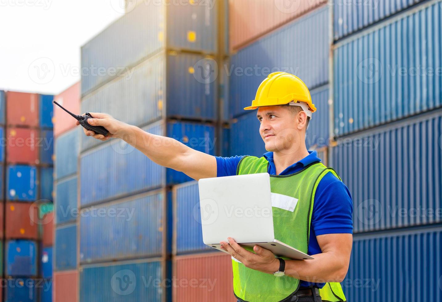 Foreman worker in hard hat and safety vest smiling and pointing control loading containers box from cargo photo
