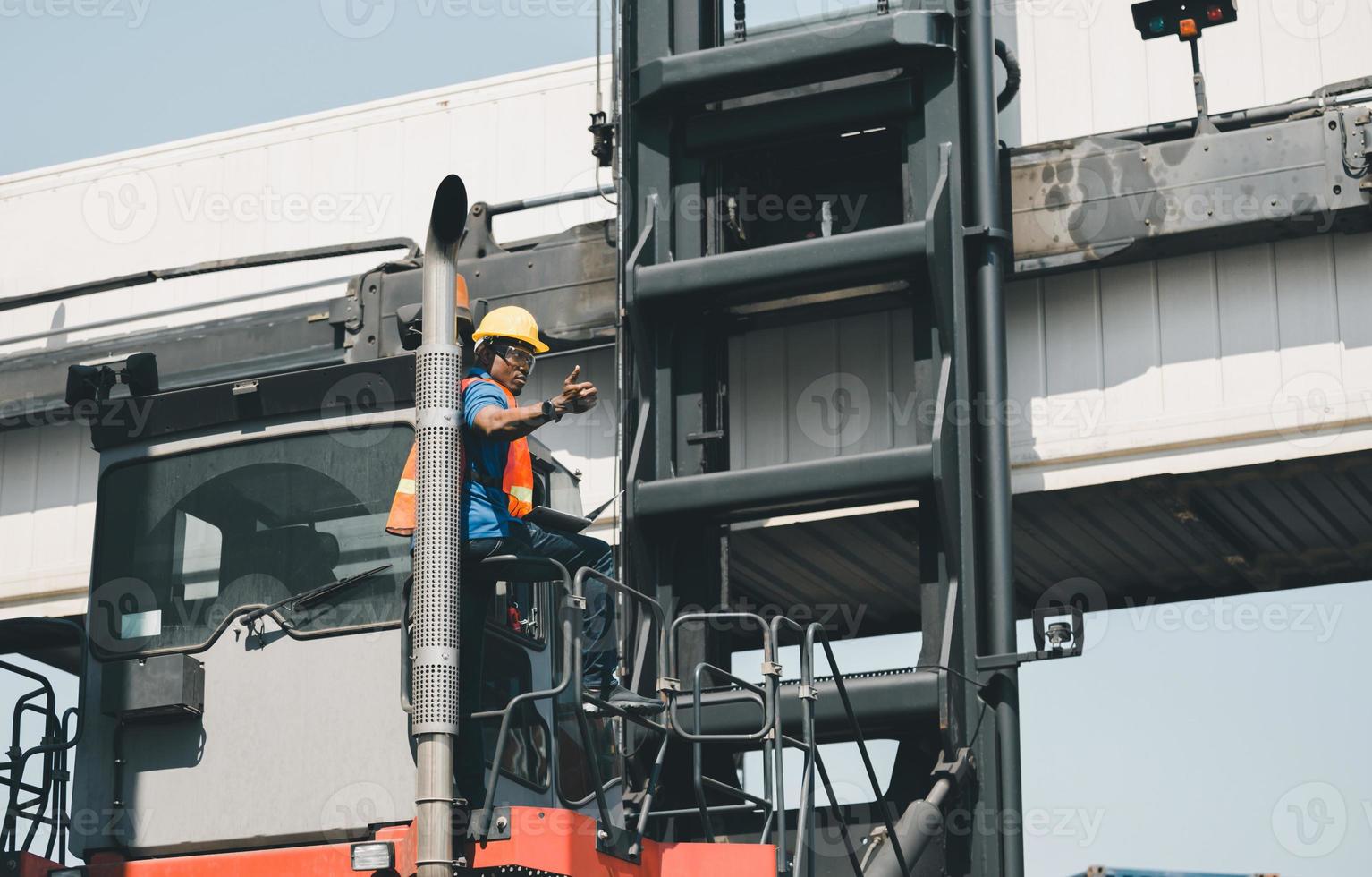 Worker man in hardhat and safety vest holding laptop standing on container stackers control loading containers box from cargo photo