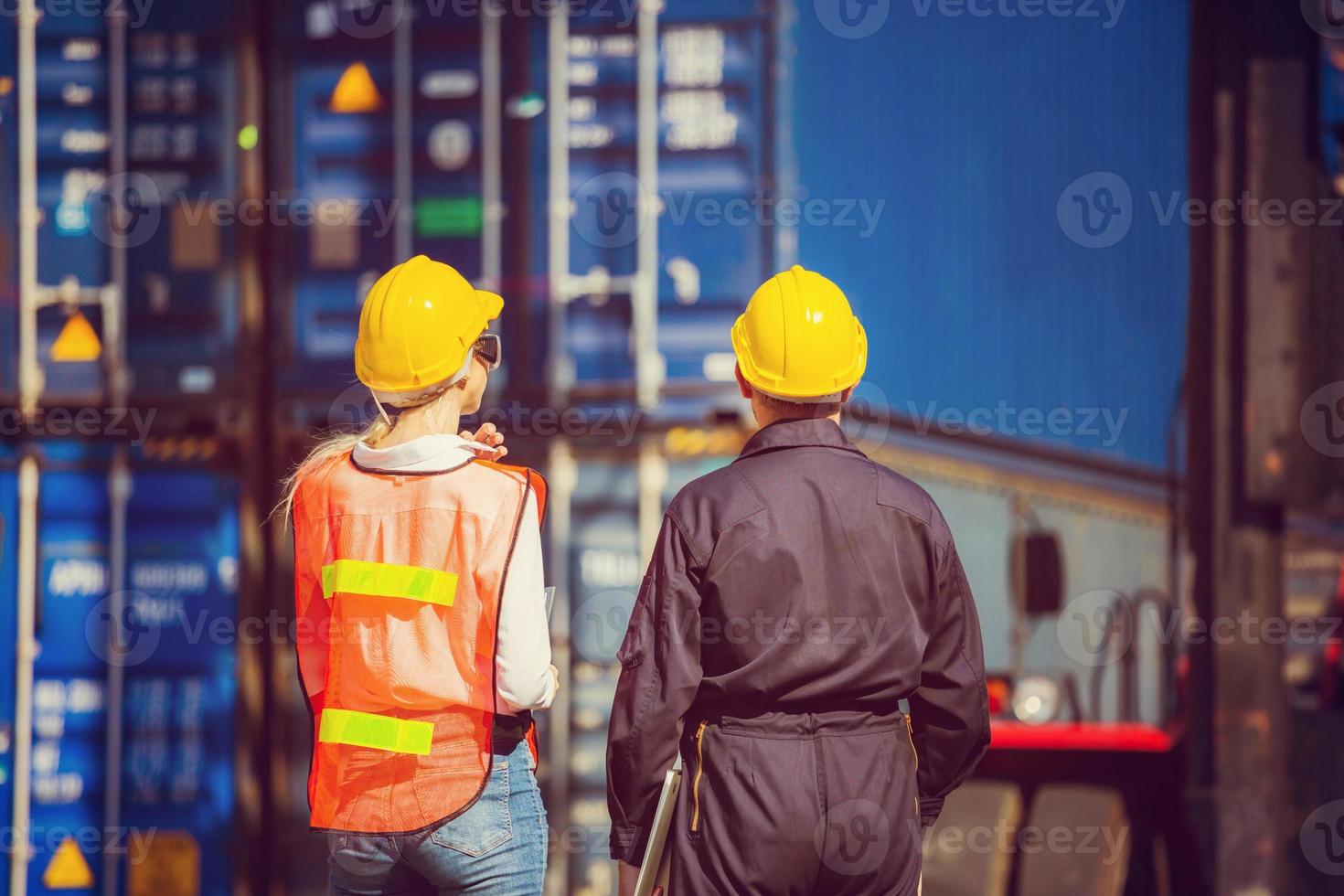 Worker man in hardhat and safety vest holding laptop and Female engineer control loading containers box from cargo photo