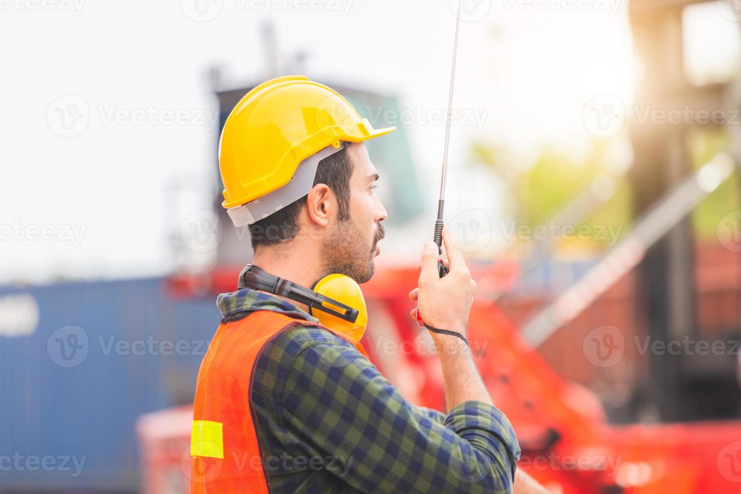 Foreman worker in hardhat and safety vest talks on two-way radio control loading containers box from cargo photo