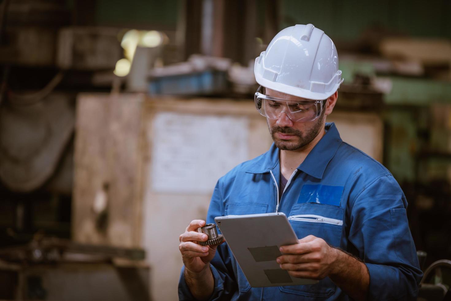 ingeniería industrial con control uniforme de seguridad que opera la máquina rectificadora de torno controlada por computadora que trabaja en la fábrica de la industria. foto