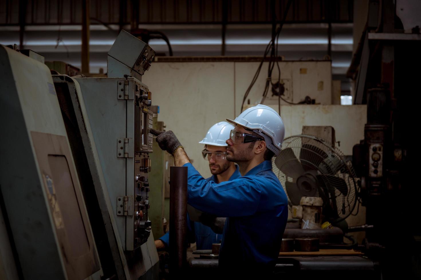 ingeniería industrial con control uniforme de seguridad que opera la máquina rectificadora de torno controlada por computadora que trabaja en la fábrica de la industria. foto