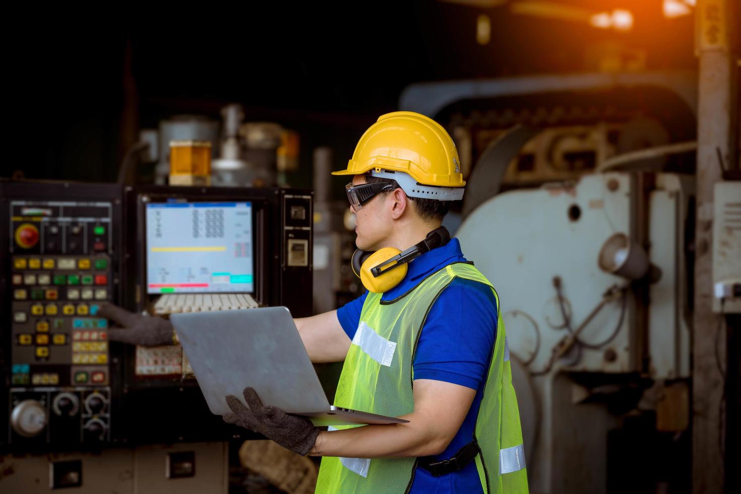 ingeniería industrial con control uniforme de seguridad que opera la máquina rectificadora de torno controlada por computadora que trabaja en la fábrica de la industria. foto