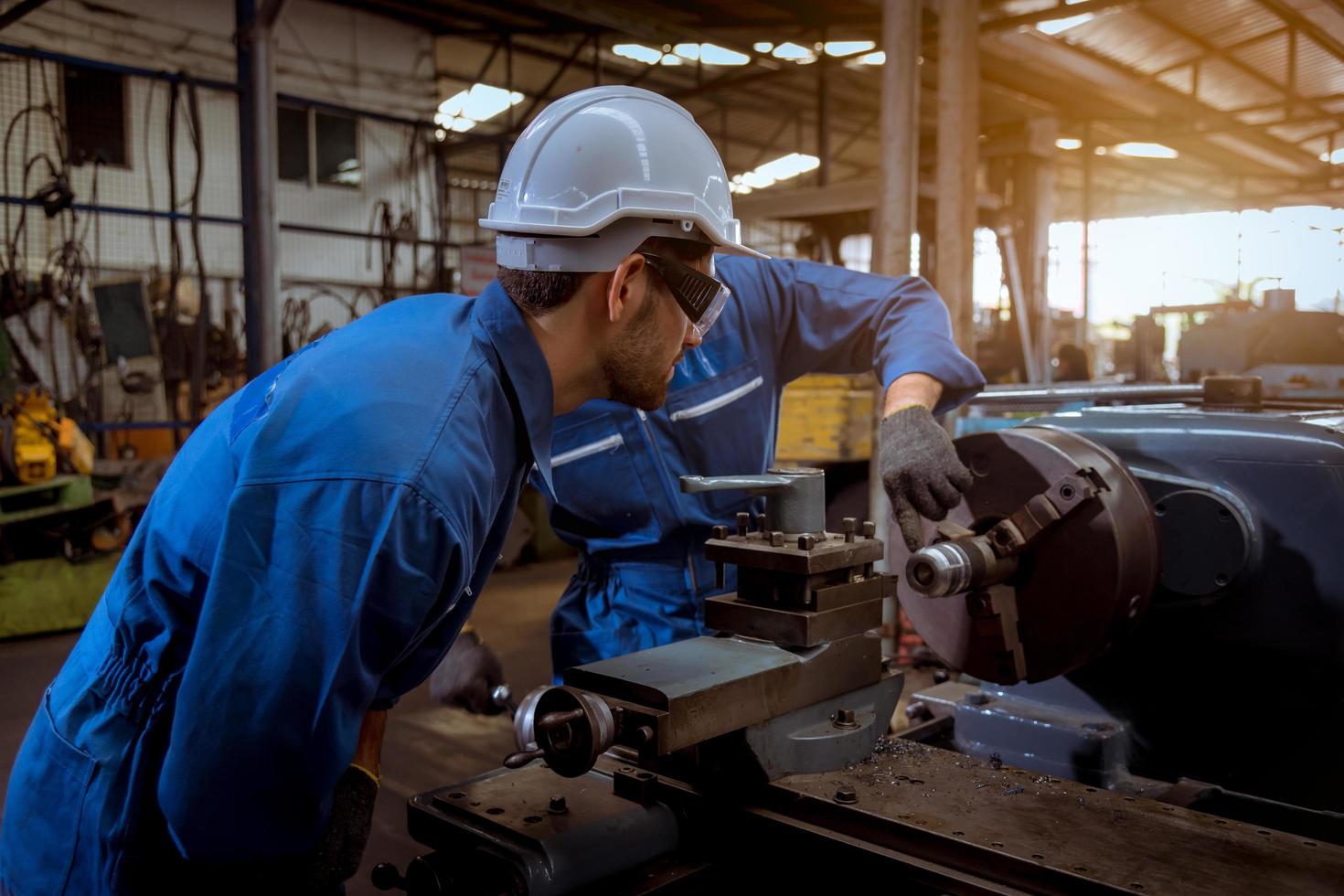 ingeniería industrial con control uniforme de seguridad que opera la máquina rectificadora de torno controlada por computadora que trabaja en la fábrica de la industria. foto