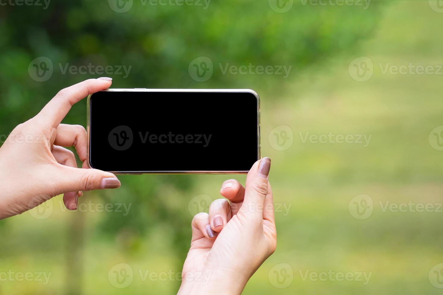 manos de mujer sosteniendo un teléfono inteligente mientras está de pie en un jardín foto