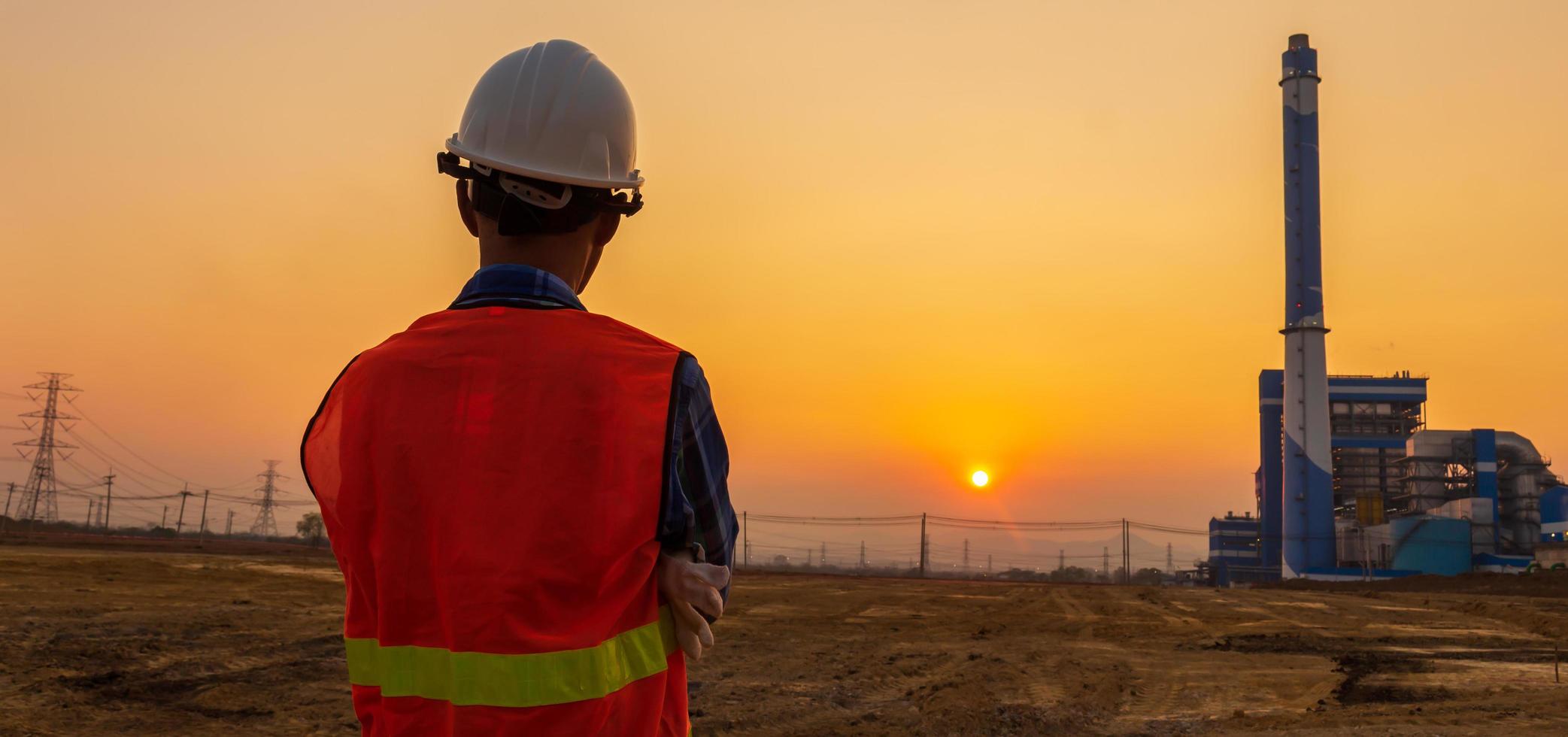 detrás de un ingeniero o trabajador con un sombrero blanco parado en un lugar de trabajo al atardecer. foto