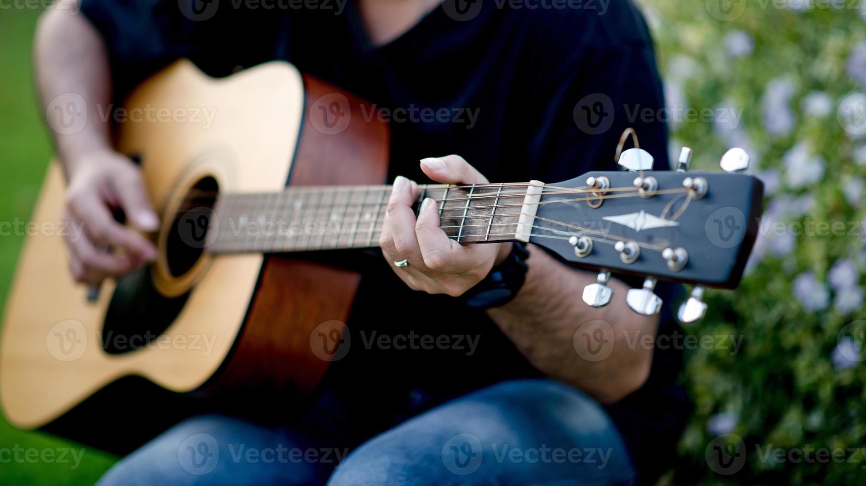 Picture of a guitarist, a young man playing a guitar while sitting in a natural garden,music concept photo