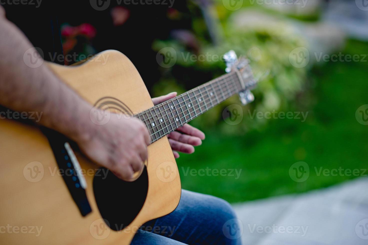 Picture of a guitarist, a young man playing a guitar while sitting in a natural garden,music concept photo