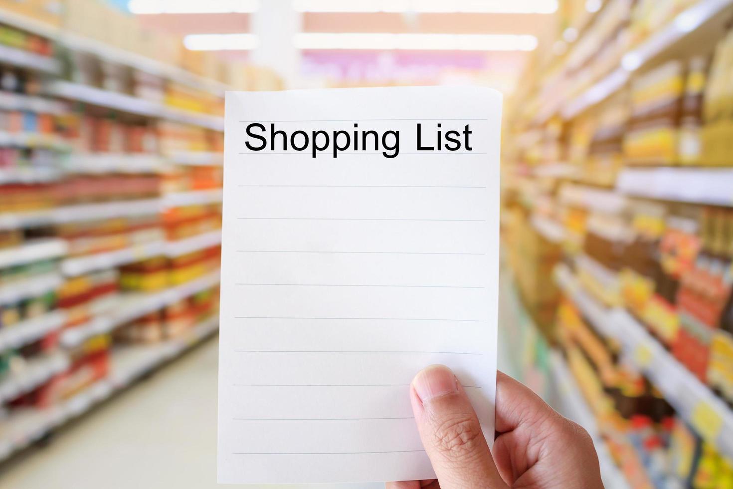 Hand holding shopping list over supermarket blur background photo