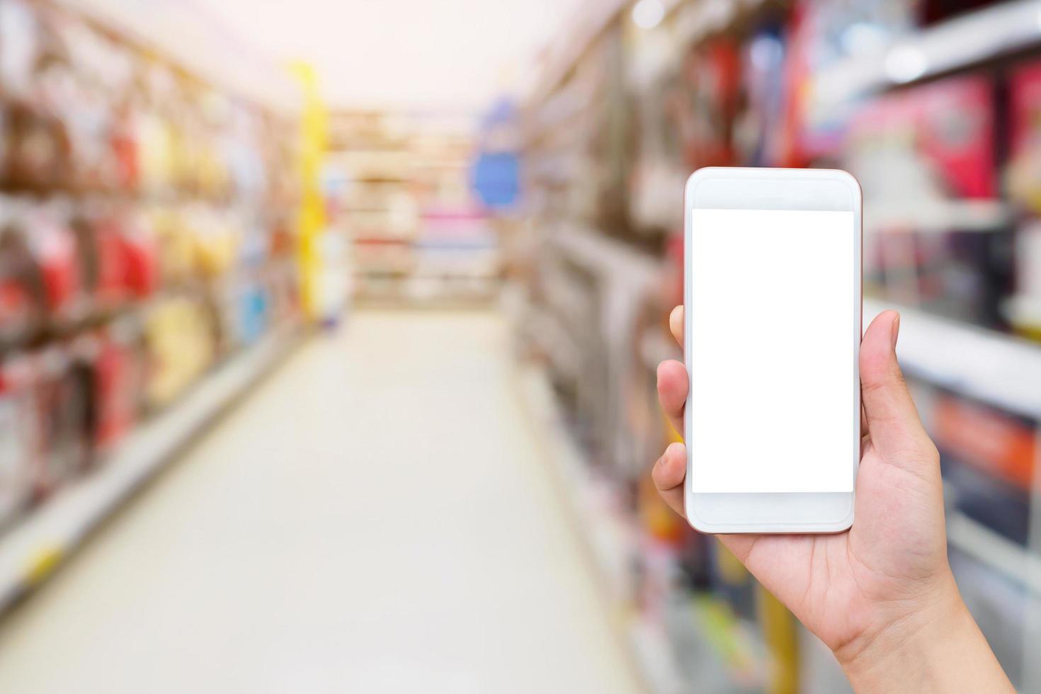 mano femenina sosteniendo un teléfono inteligente móvil en el fondo del pasillo del supermercado foto