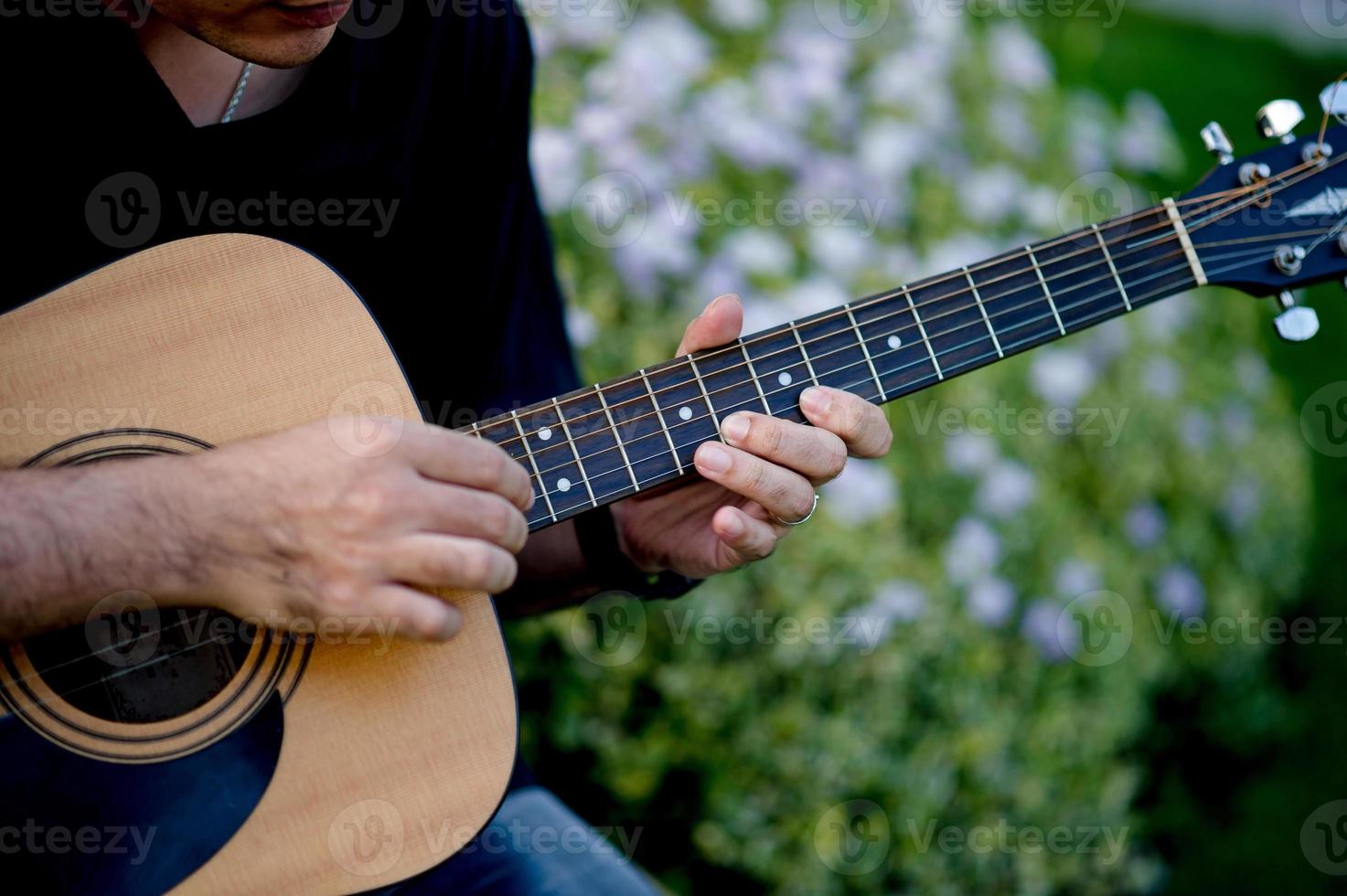 Picture of a guitarist, a young man playing a guitar while sitting in a natural garden,music concept photo