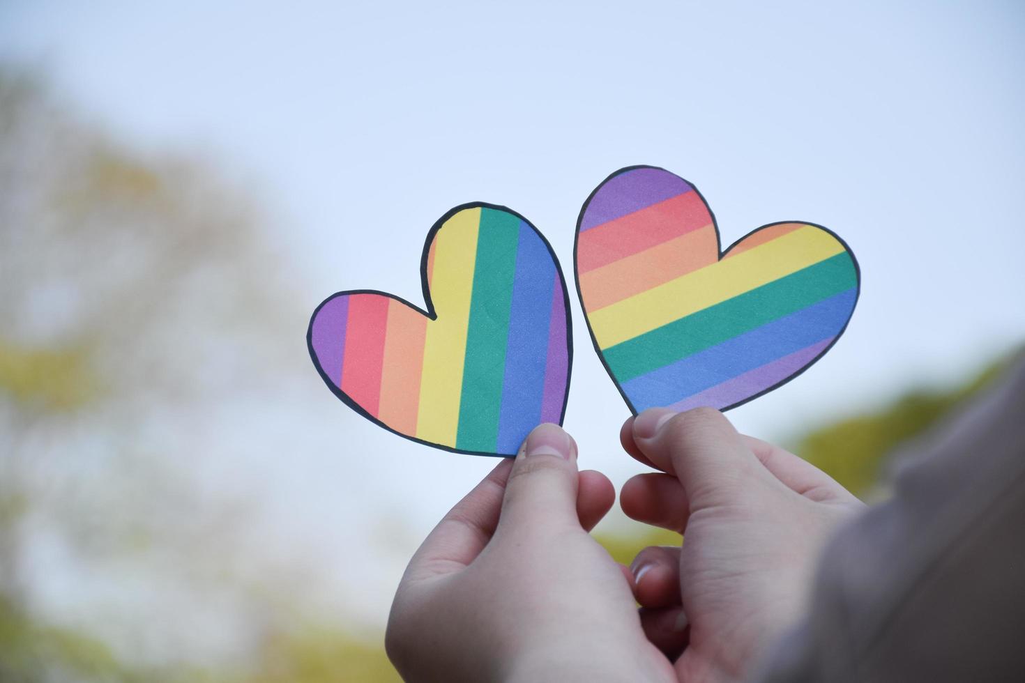 Two hearts made of rainbow colored paper are holding in hands of the LGBT person, concept for lgbtq communities celebrations in pride month around the world photo