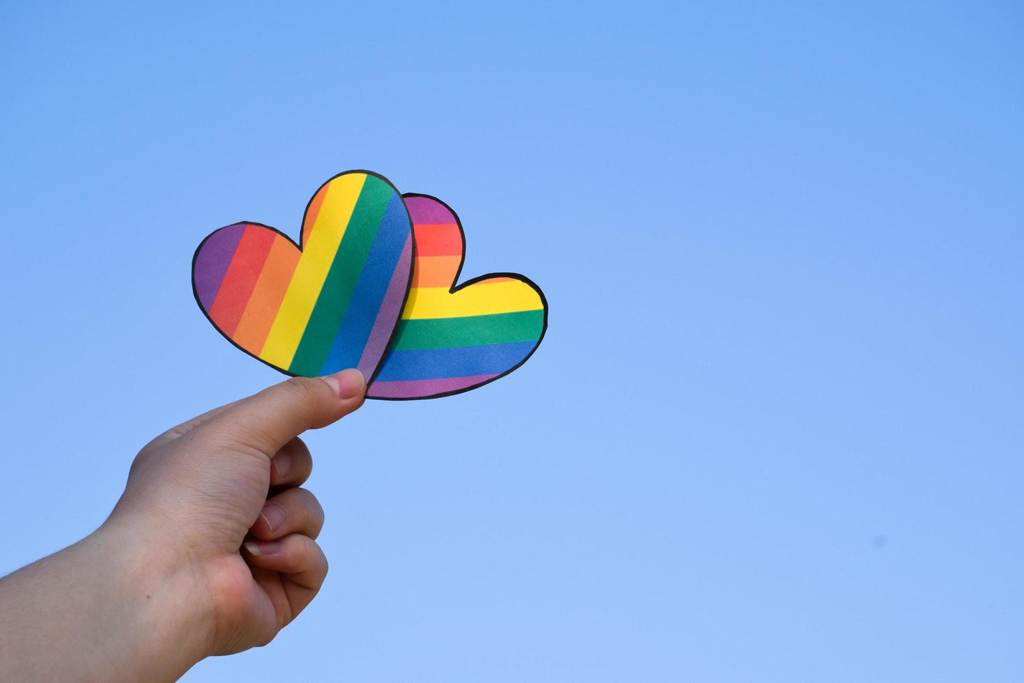 dos corazones hechos de papel de color arcoiris se sostienen en las manos de la persona lgbt, concepto para las celebraciones de las comunidades lgbtq en el mes del orgullo en todo el mundo foto