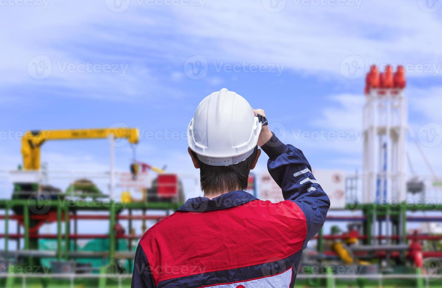 Rear view of young engineer in blue mechanic jumpsuit wearing white safety helmet before working on oil tanker ship at shipyard photo