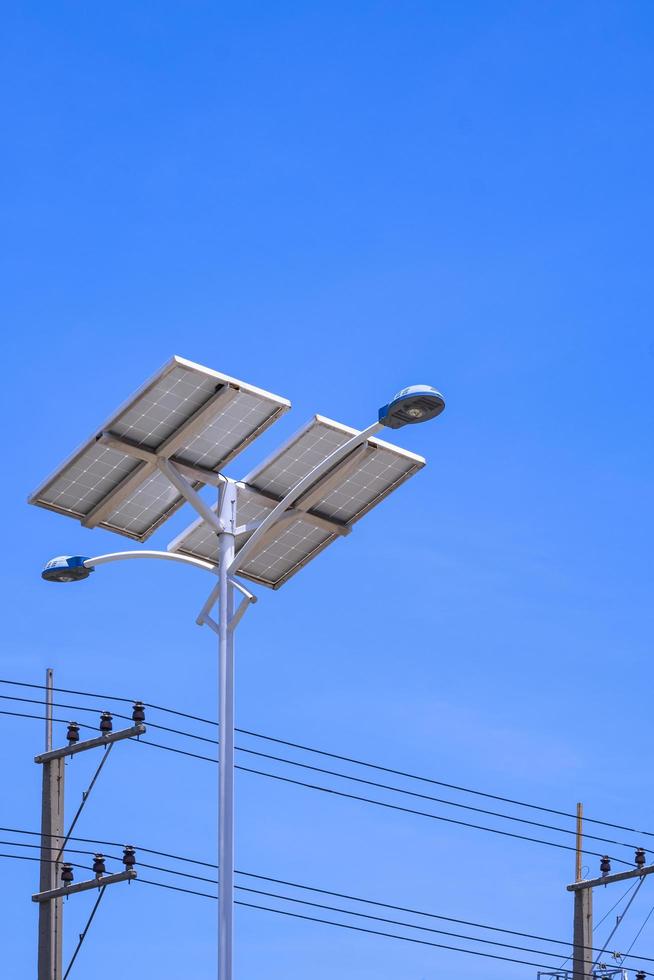 Low angle view of streetlight post and solar power panel with electric poles against blue clear sky in vertical frame photo
