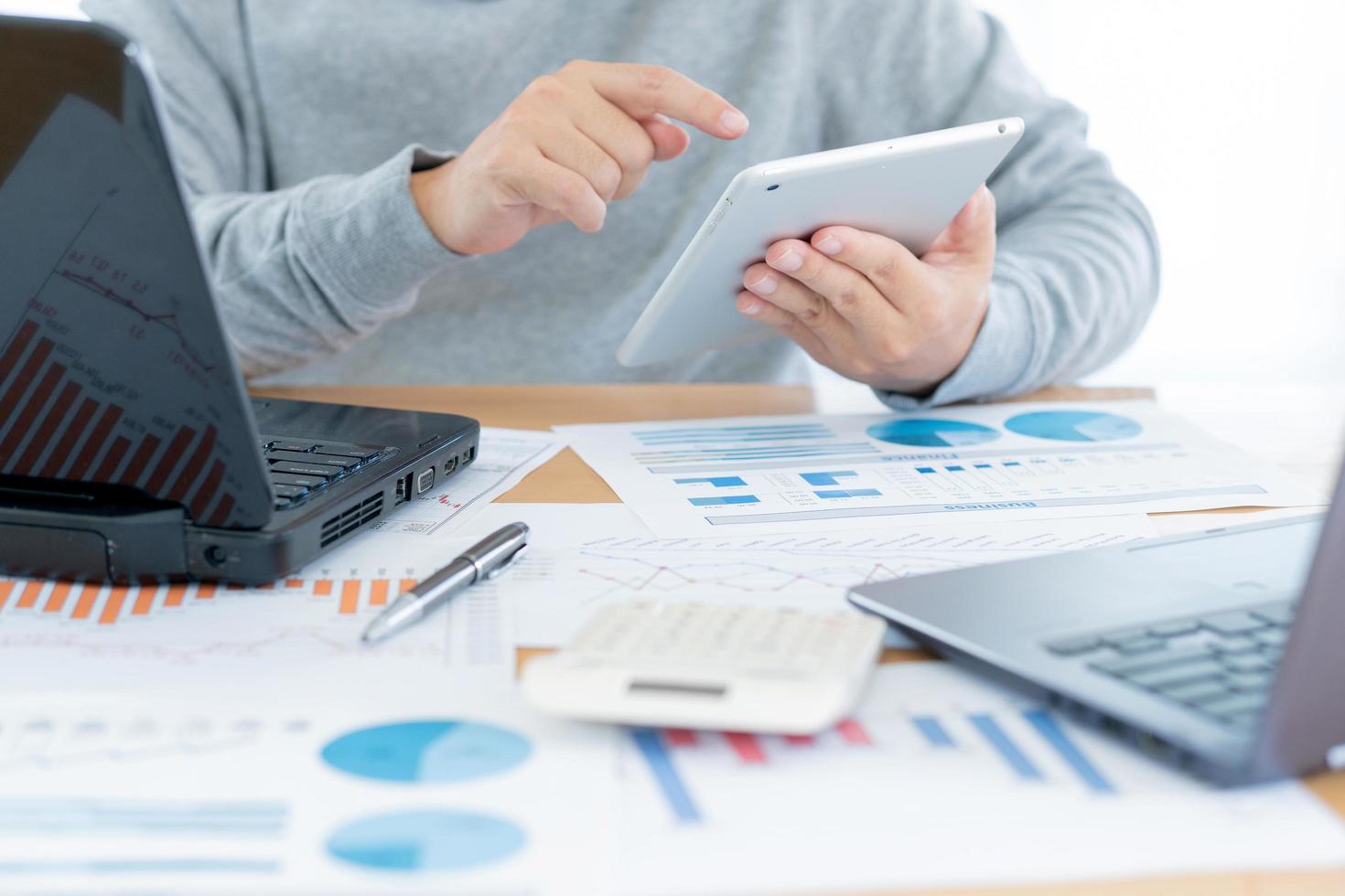 Businessman hand holding tablet working to analysis business data, finance document with laptop computer on desks, concept photo