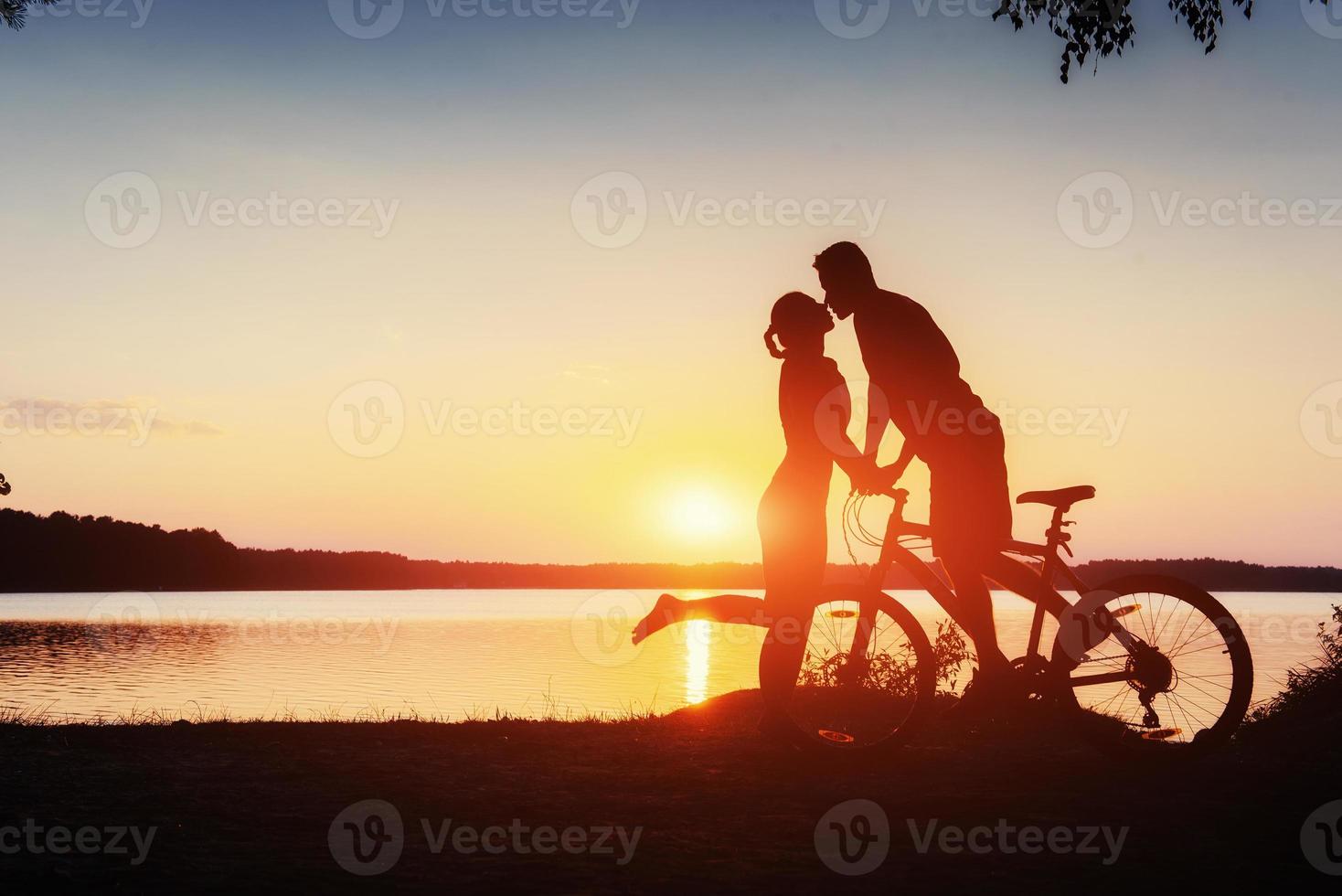 couple on a bicycle at sunset by the lake photo