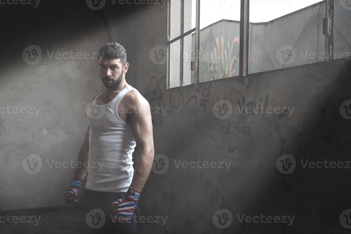 boxeador musculoso parado cerca de la ventana en un edificio abandonado. foto