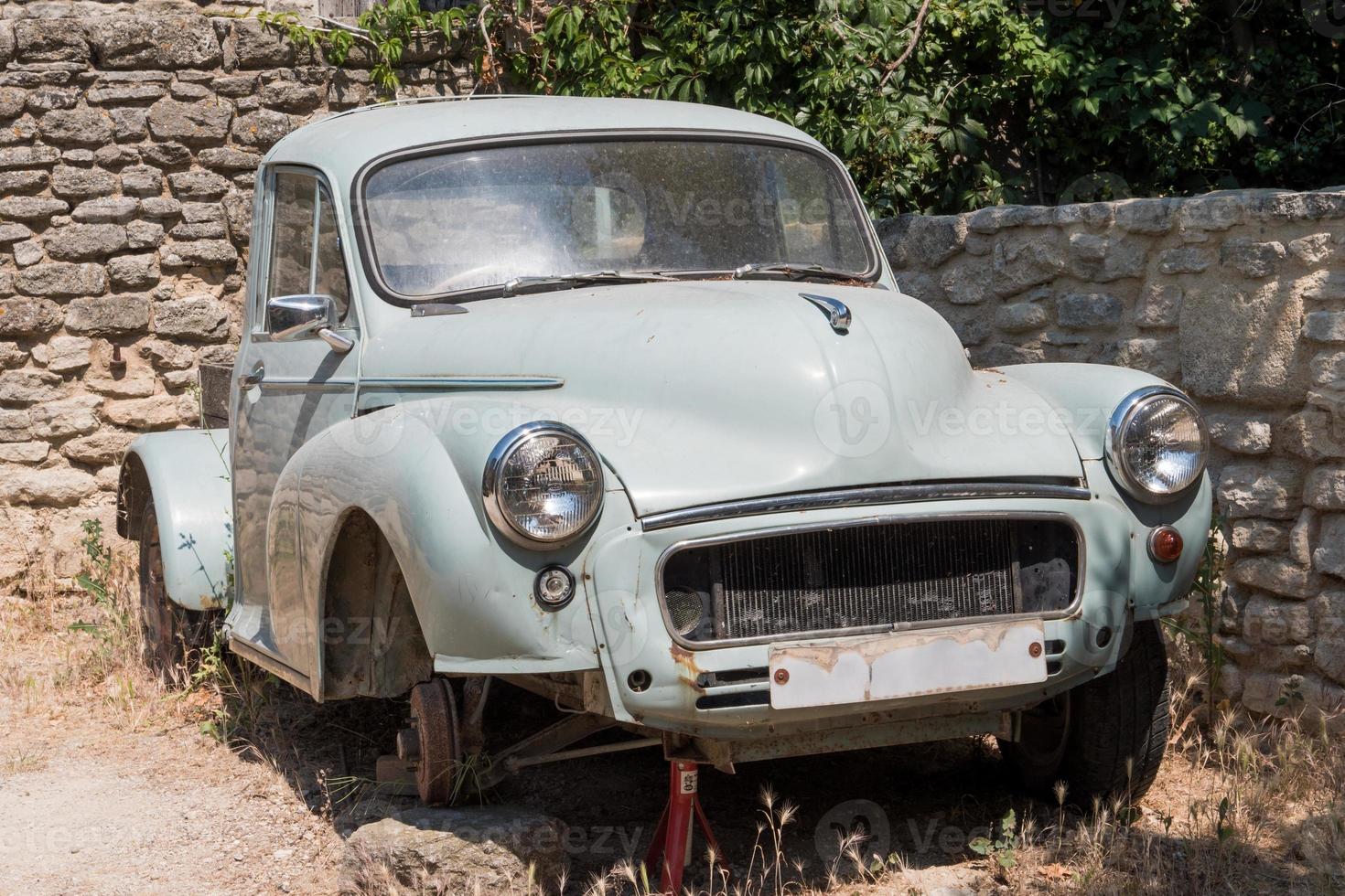 Old abandoned pick-up rusting near stone wall. photo