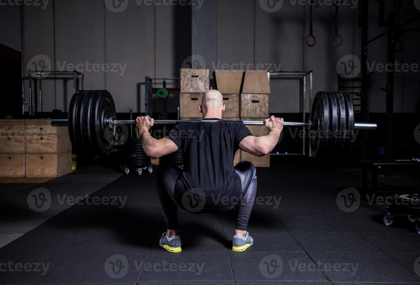 hombre musculoso atlético levantando pesas y haciendo sentadillas en el gimnasio. gradación de color espectacular. foto