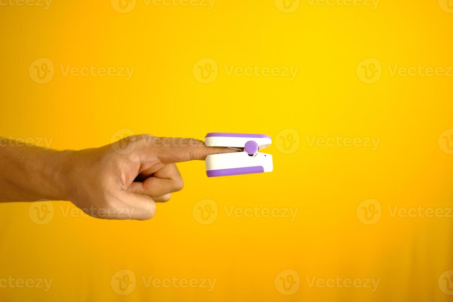 close up of man hand using pulse oximeter against yellow background photo