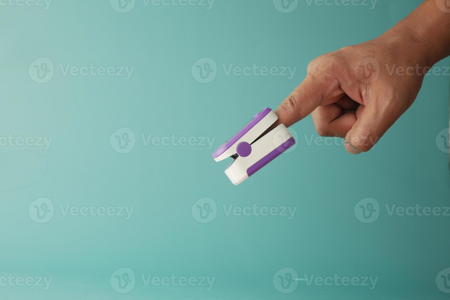 close up of man hand using pulse oximeter against light green background photo