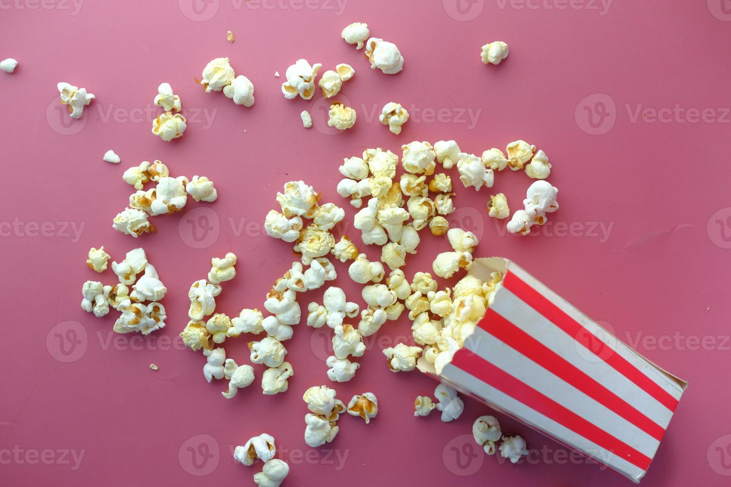 Palomitas de maíz derramándose de un recipiente sobre fondo rojo. foto