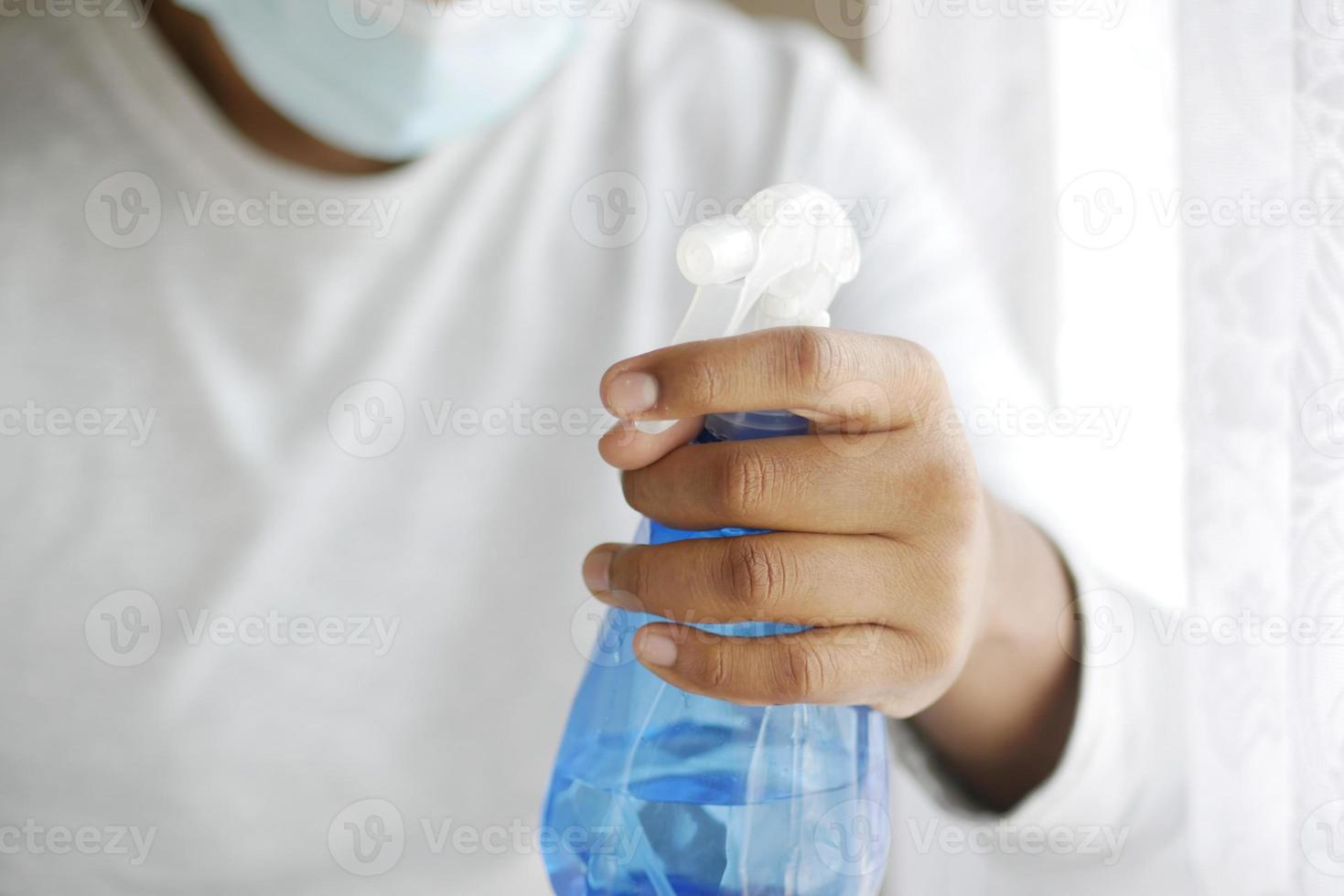 Mano en guantes de goma azul sosteniendo una botella de spray con espacio de copia foto