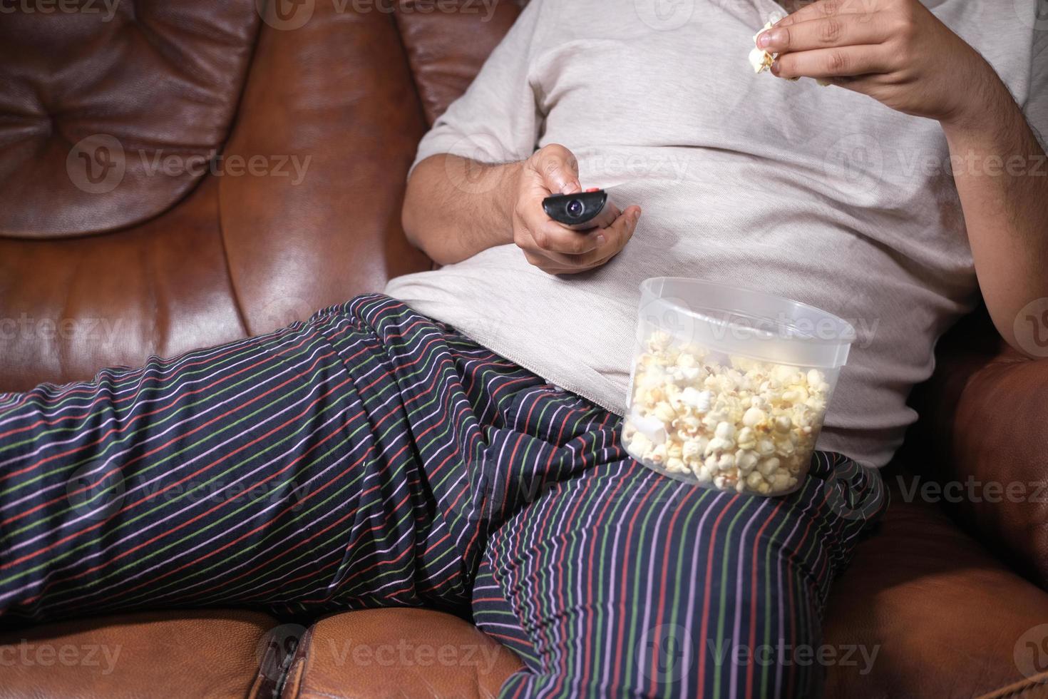 a lazy man holding tv remote and eating popcorn photo