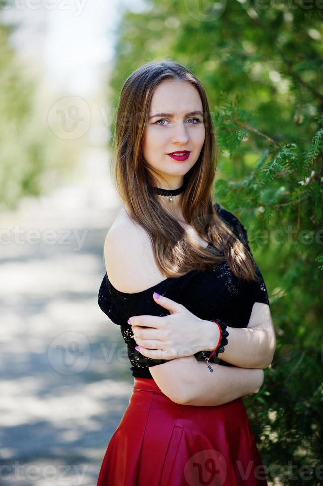 Portrait of girl with bright make up with red lips, black choker necklace on her neck and red leather skirt. photo