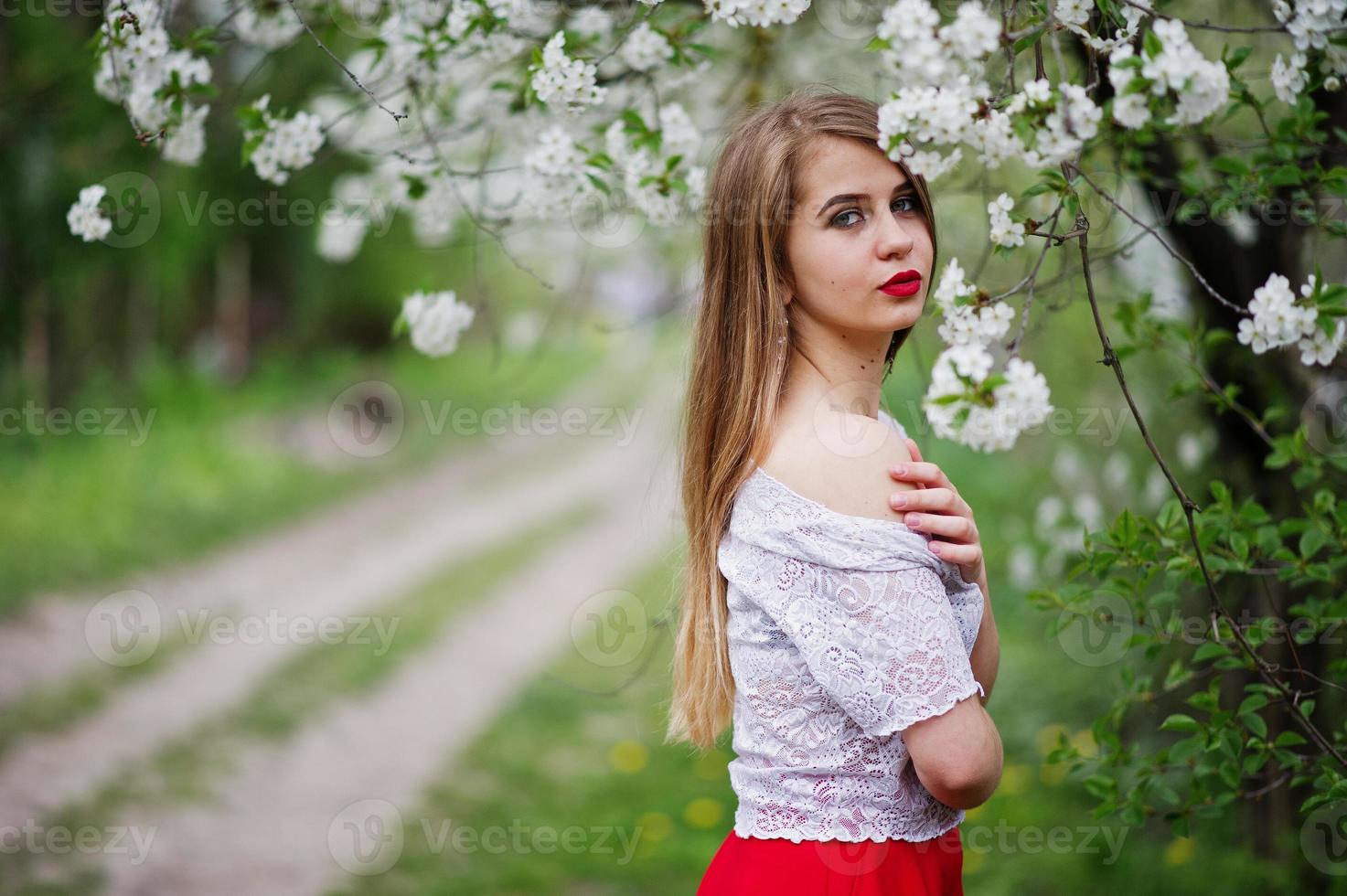 Portrait of beautiful girl with red lips at spring blossom garden, wear on red dress and white blouse. photo