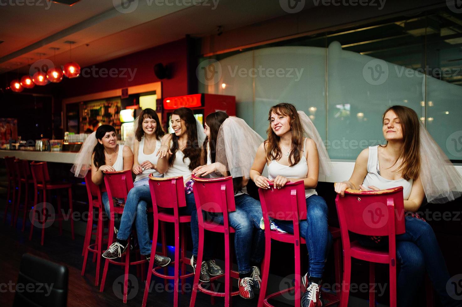 seis chicas con velo se sientan en los taburetes de la barra en la despedida de soltera. foto