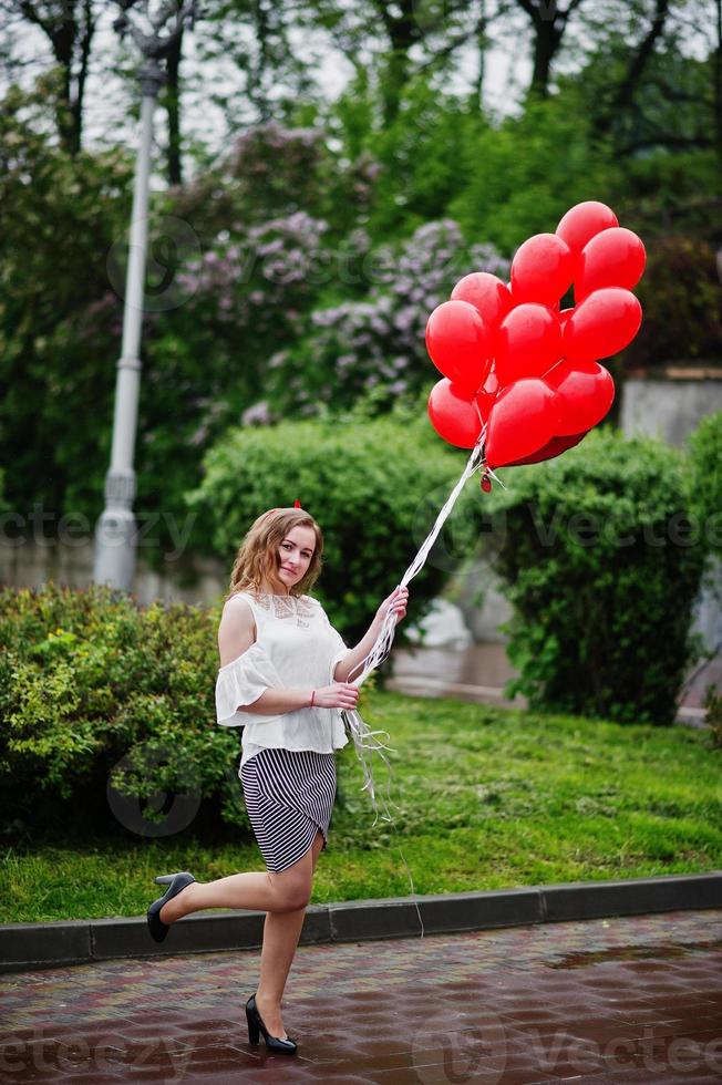 Portrait of a gorgeous beautiful bridesmaid in a pretty dress holding heart-shaped red balloons in the park at bachelorette party. photo