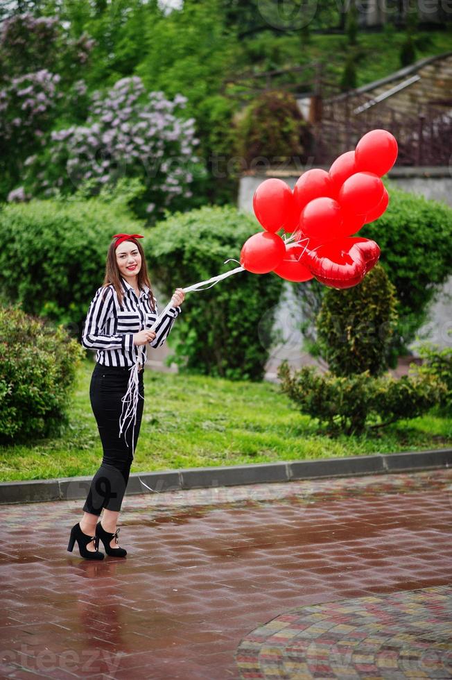 Portrait of a gorgeous beautiful bridesmaid in casual clothes holding heart-shaped red balloons in the park at bachelorette party. photo