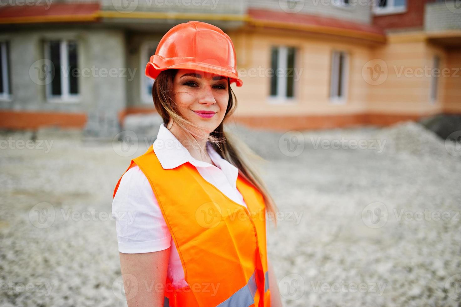 mujer ingeniera constructora con chaleco uniforme y casco protector naranja contra el nuevo edificio. tema de bloque de vivienda de propiedad. foto